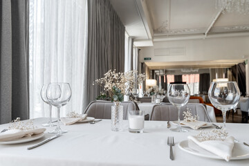 beautiful table decoration in restaurant. festive table setting in restaurant. white tablecloth on table, wine glasses, white plates, flowers in vase, candles are burning. romantic atmosphere