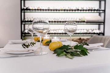 beautiful table decoration in restaurant. festive table setting in restaurant. white tablecloth on table, wine glasses, white plates, lemons, candles are burning. romantic atmosphere