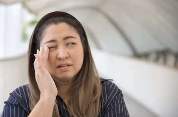 Chubby Asian middle aged woman suffering from irritated eye, concept image for optical health care,...