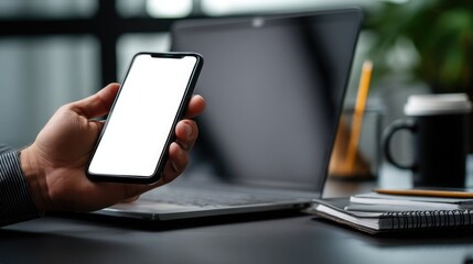 Close-up of a businessman holding a smartphone while using a laptop at his desk in the office. Close-up of hands with a phone and computer on the table, a business concept