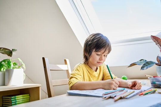 Boy drawing with colored pencils at home near a window - Powered by Adobe