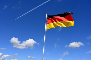 The german flag flutters in the wind an aeroplane flies past at high altitude with a contrail