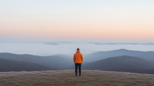 Solitude on a mountaintop at sunrise.  A person stands alone, contemplating the vastness of a misty mountain landscape