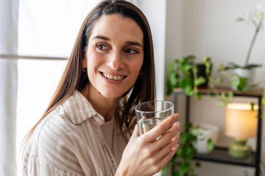 Woman smiling indoors holding a glass of water