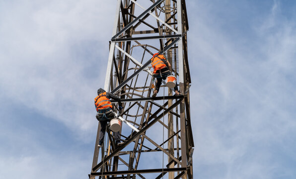 Two rope access painters, industrial climbers working at height. Industrial climbing for painting, repair work, and maintenance of a metal transmission or lattice tower by workers.