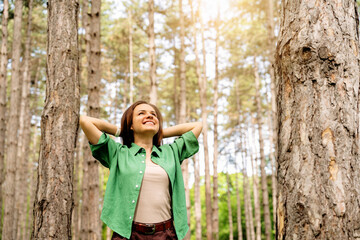 Happy woman with hands behind her head enjoying walking in forest.