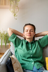 Portrait of serene woman with hands behind head and closed eyes relaxing on sofa at home