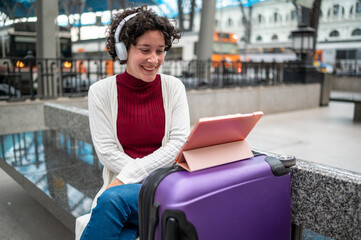 Tourist woman listening music using headphones and watching tablet while waiting train