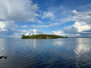 Island with lush greenery and a red house, surrounded by water. in Sweden.
