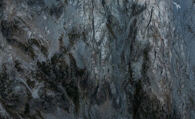 Close-up view of textured, dark gray rock face with crevices and varied tones