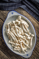 Raw white shimeji mushrooms in bowl on wooden table. Top view.
