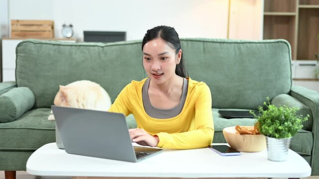 Woman relaxing on sofa at home with dog reading digital tablet in bright modern living room, joyful pet