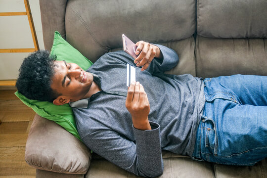 Happy young man holding credit card and smartphone, enjoy easy fast secure transferring money in e-banking app