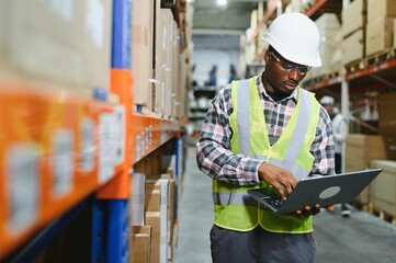 African american Warehouseman checking delivery, stock in warehouse on laptop. Warehouse manager...