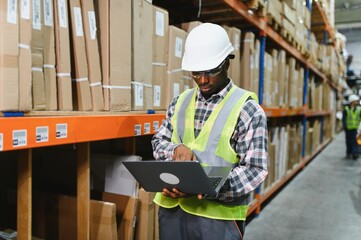 African american Warehouseman checking delivery, stock in warehouse on laptop. Warehouse manager...