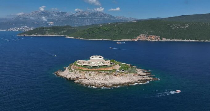 Small island with historic Mamula fort in blue sea, surrounded by boats and mountains