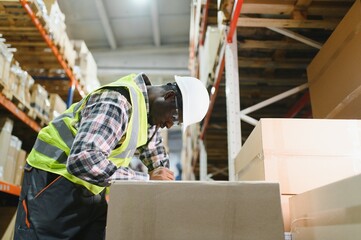 African american warehouseman with clipboard checking delivery, stock in warehouse