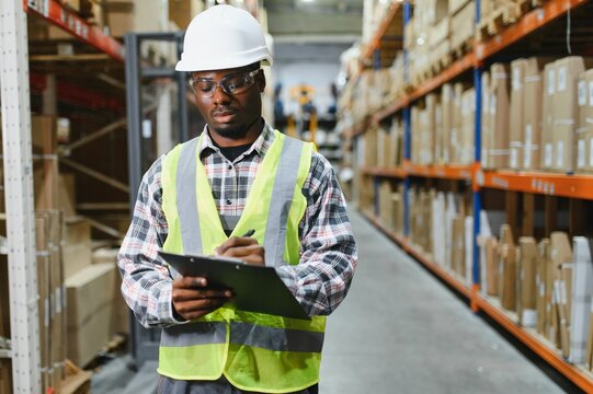 Portrait of african american warehouseman with clipboard checking delivery, stock in warehouse. Warehouse worker preparing products for shipment