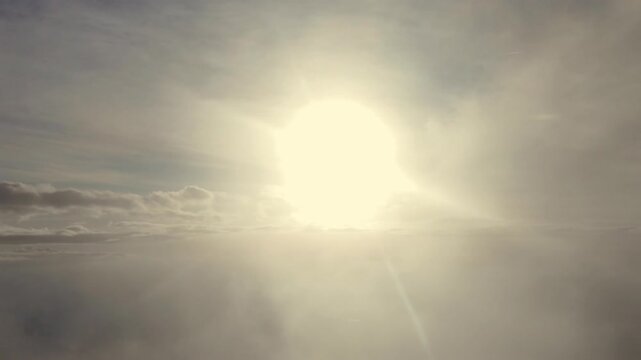 an immersive pilot&rsquo;s perspective from a jet cokpit flying westbound at sunset through layers of ethereal clouds, with a blinding sun shining ahead over the horizon