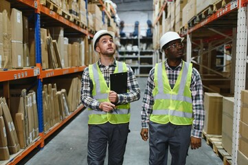 Two warehouse workers are walking through the facility, engaged in conversation about logistics, supply chain management, and inventory