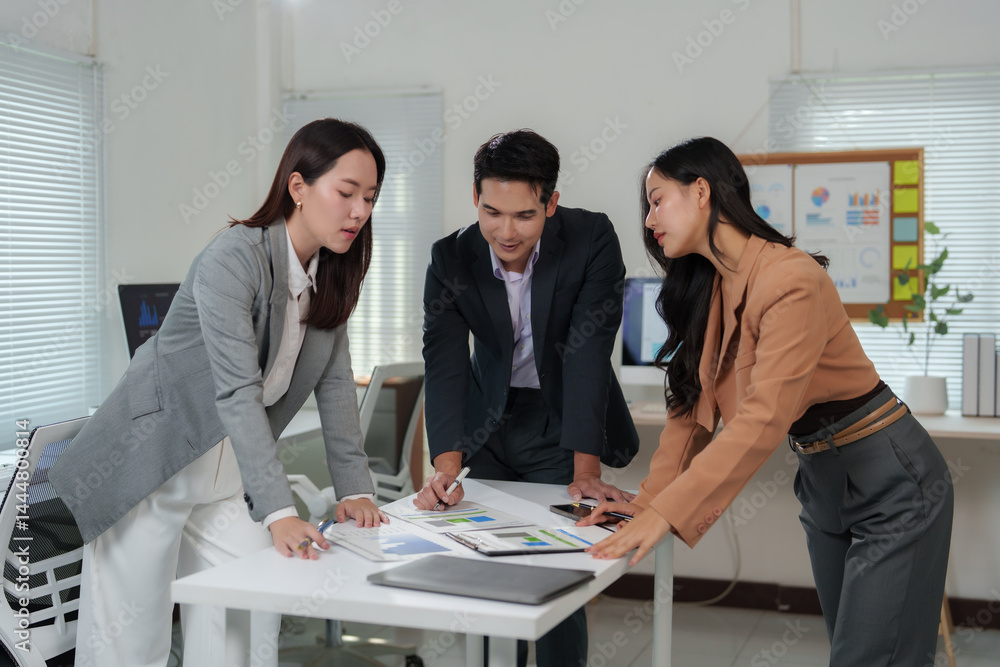Poster three asian businesspeople are having a meeting in a modern office, examining charts and graphs disp