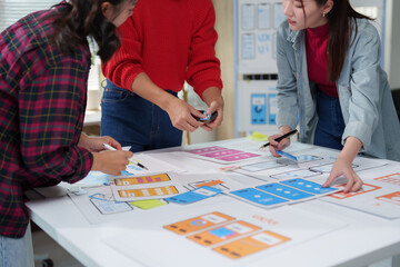 Web designers are collaborating on user experience design for a mobile app, meticulously arranging...
