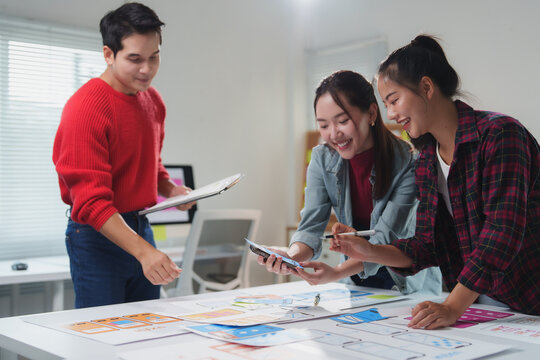 Three asian web designers are collaborating on a project. Analyzing mobile app layouts and uiux designs. Combining their expertise to create a user friendly and visually appealing mobile application