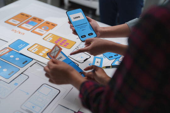 Two ux designers collaborating on a project, arranging wireframes and discussing user interface design for a mobile app, showcasing the creation of user friendly digital experiences