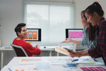 Asian uiux designers collaborating and discussing mobile app interface wireframe designs in a...