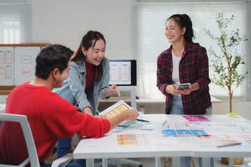 Diverse group of young professionals engaging in a brainstorming session for a mobile app design. They are gathered around a table covered with design sketches and digital devices