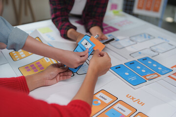 Web designers are working together to develop user interface and user experience by adding paper...