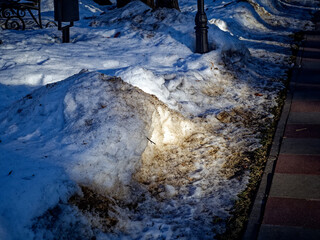 Street lamp pole in a snowdrift of dirty snow