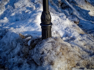 Street lamp pole in a snowdrift of dirty snow