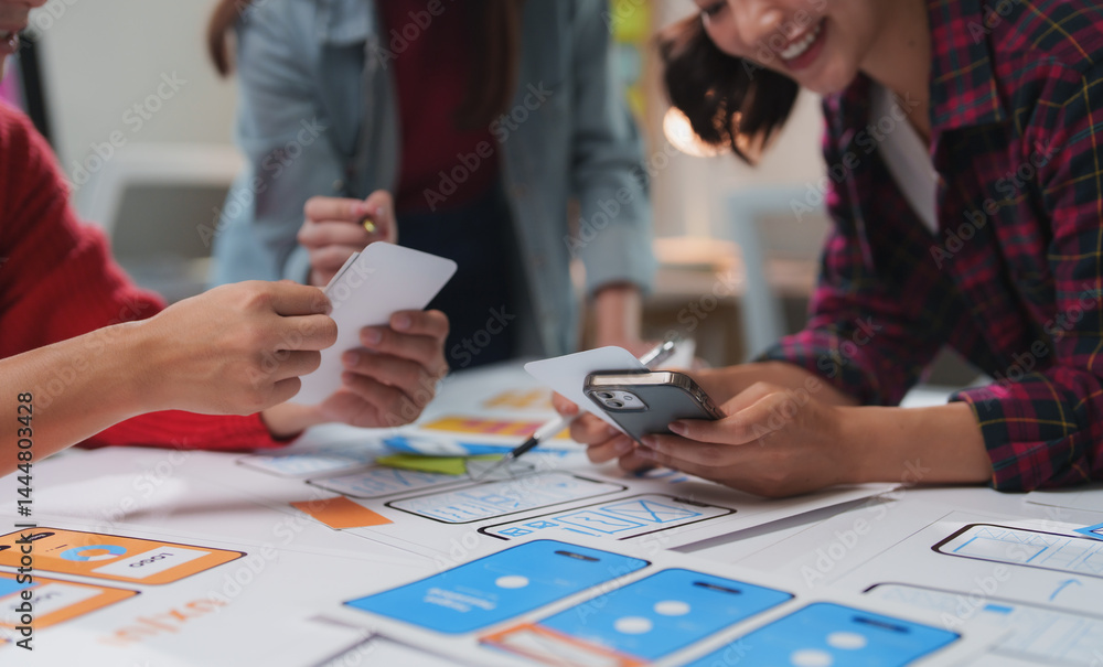 Poster asian ux designers are comparing mobile phone app wireframes and discussing new features during a pr