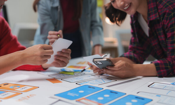 Asian ux designers are comparing mobile phone app wireframes and discussing new features during a productive meeting, focusing on user experience and interface design