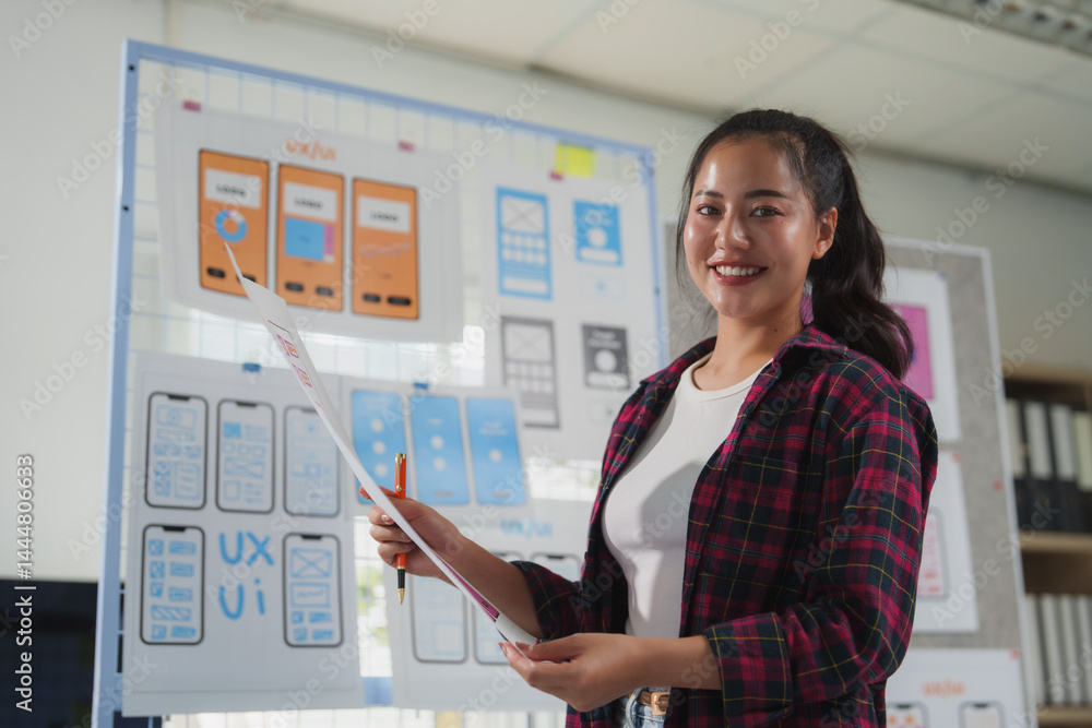 Poster asian female web designer smiling and holding wireframe of mobile application in the office, she is 