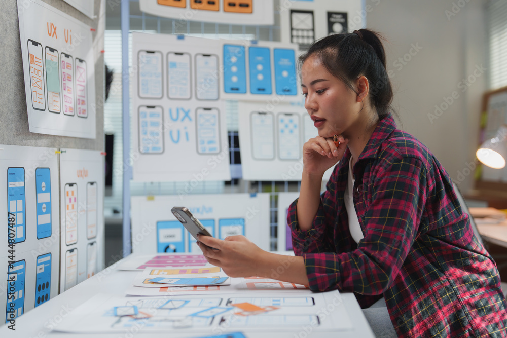 Poster female uxui designer comparing wireframe sketches of a mobile application on a smartphone and paper 