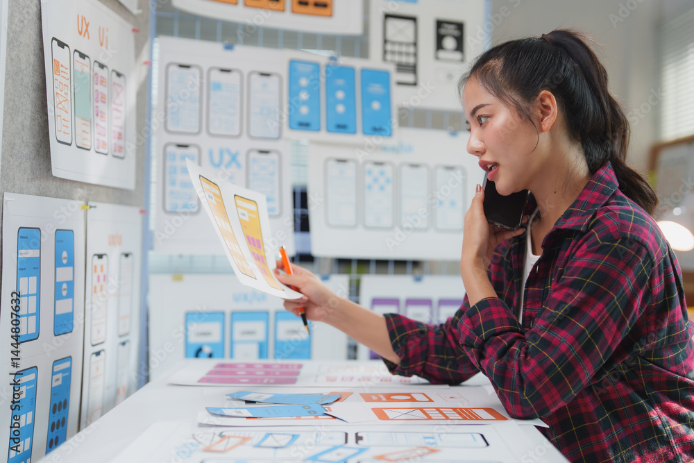Poster young asian woman working as a ux ui designer, engaging in a phone conversation while discussing the