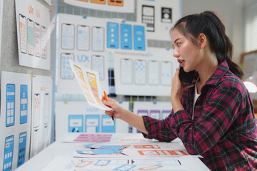 Young asian woman working as a ux ui designer, engaging in a phone conversation while discussing...