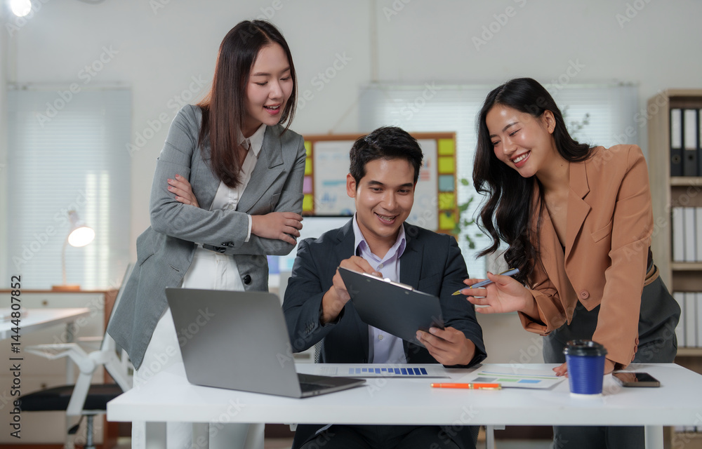 Poster three happy asian businesspeople are smiling and collaborating on a project, using documents and a l