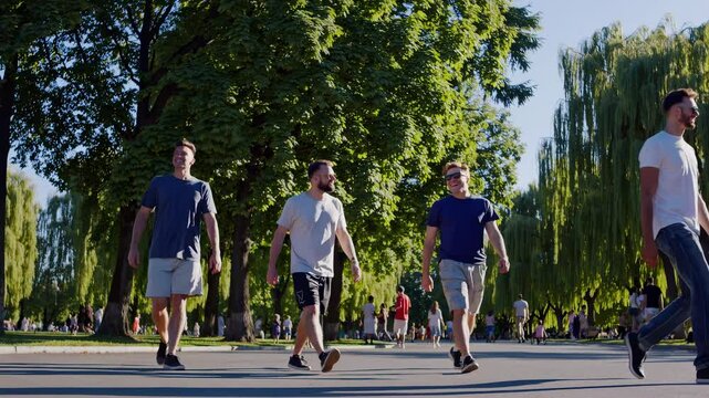 Wide-angle video shot of four men walking in a sunlit park, surrounded by lush trees, capturing a relaxed, casual outdoor vibe.
