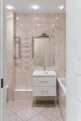 small bathroom with white bathtub, white sink, square mirror, cabinet under sink, chrome faucet.  ceramic tiles on walls. Bathroom design in flat, hotel or apartment.