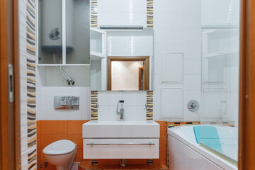bathroom design with white bright orange tiles, white sink, mirror, white pedestal under the sink, toilet and bathtub.