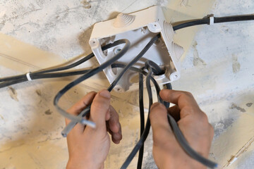 Electrician is working on electrical wiring, carefully connecting wires to a junction box during a home renovation or installation project