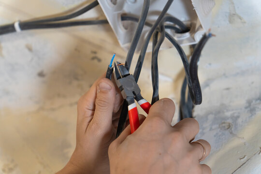Electrician using pliers to skillfully cut and strip electrical wires, engaging in vital maintenance and installation work to ensure safe and efficient connections within the electrical system
