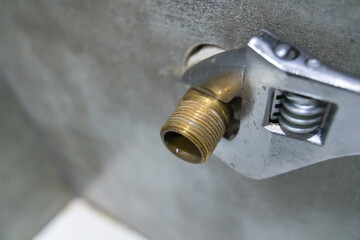 Adjustable wrench gripping a brass pipe fitting during plumbing work, showcasing the tools and materials used in plumbing and home repair