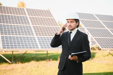Caucasian engineer using smartphone while standing with solar panel at the background. Concept of...