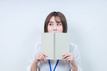 顔の前にノートをかざしたカメラ目線の女性