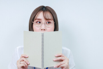 	ノートで顔を隠す眼鏡をした若い女性