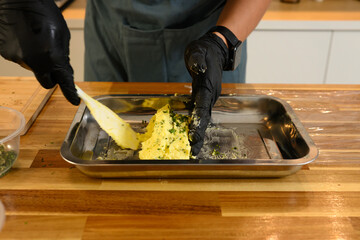 Close up of hands blending chopped herbs into softened butter on a metal tray